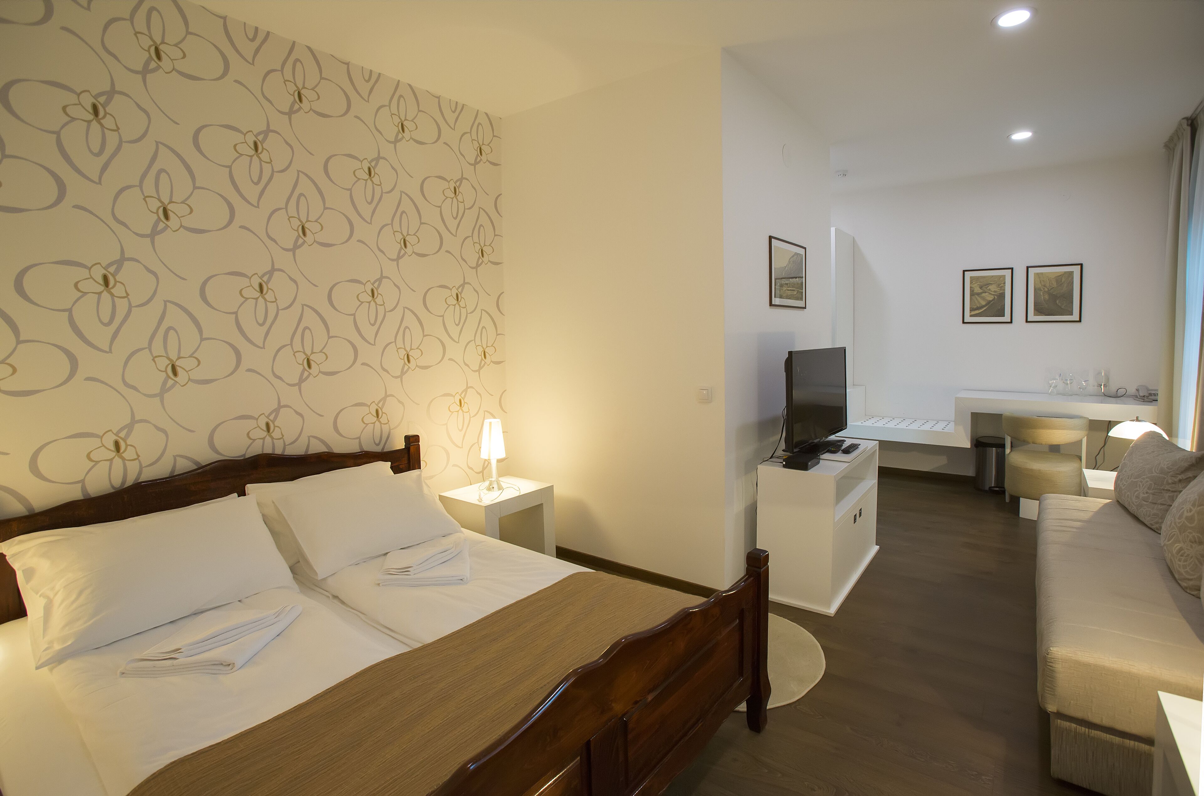 Una camera d'albergo con un letto, comodino, lampada, televisione e divano.