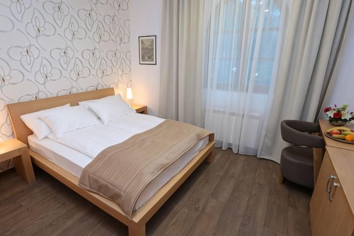 Habitación de hotel con cama de madera, una mesita de noche, un escritorio con silla y una ventana con cortinas.