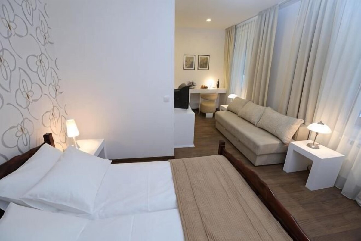 Quarto de hotel com uma cama, um sofá, uma escrivaninha e uma luminária.