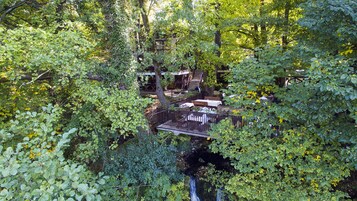 Un espacio de descanso al aire libre de estilo rústico, con mesas y bancos de madera, rodeado de abundante follaje y árboles.