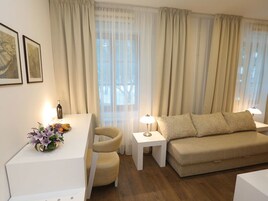 Sala de estar con sofá, una silla, una mesita y una lámpara. Hay cortinas y una ventana.