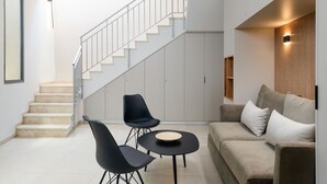 A modern living room with a staircase, a sofa, two chairs, and a small table. - Elegant Duplex with XL Patio by FeelHome (Tel Aviv)