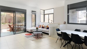 A modern living room with a sofa, coffee table, and dining table. - Elegant Duplex with XL Patio by FeelHome (Tel Aviv)