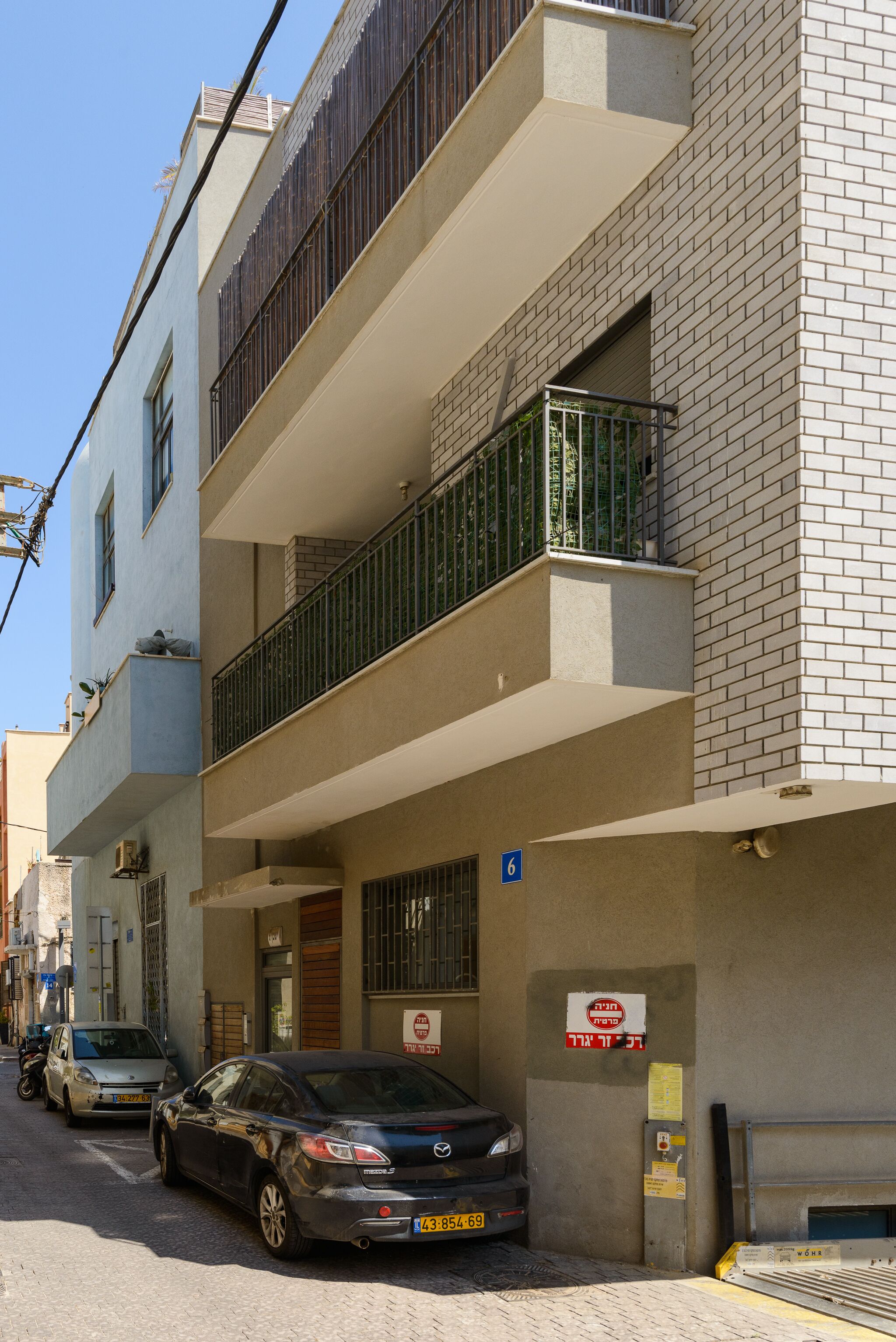 A multi-story building with a ground-level entrance, a balcony on the second floor, and a parked car in front.