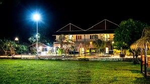 Un edificio de dos pisos con un balcón, rodeado de un jardín iluminado durante la noche.