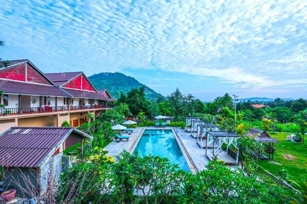 A resort with a swimming pool, multiple guest rooms, and lush greenery.