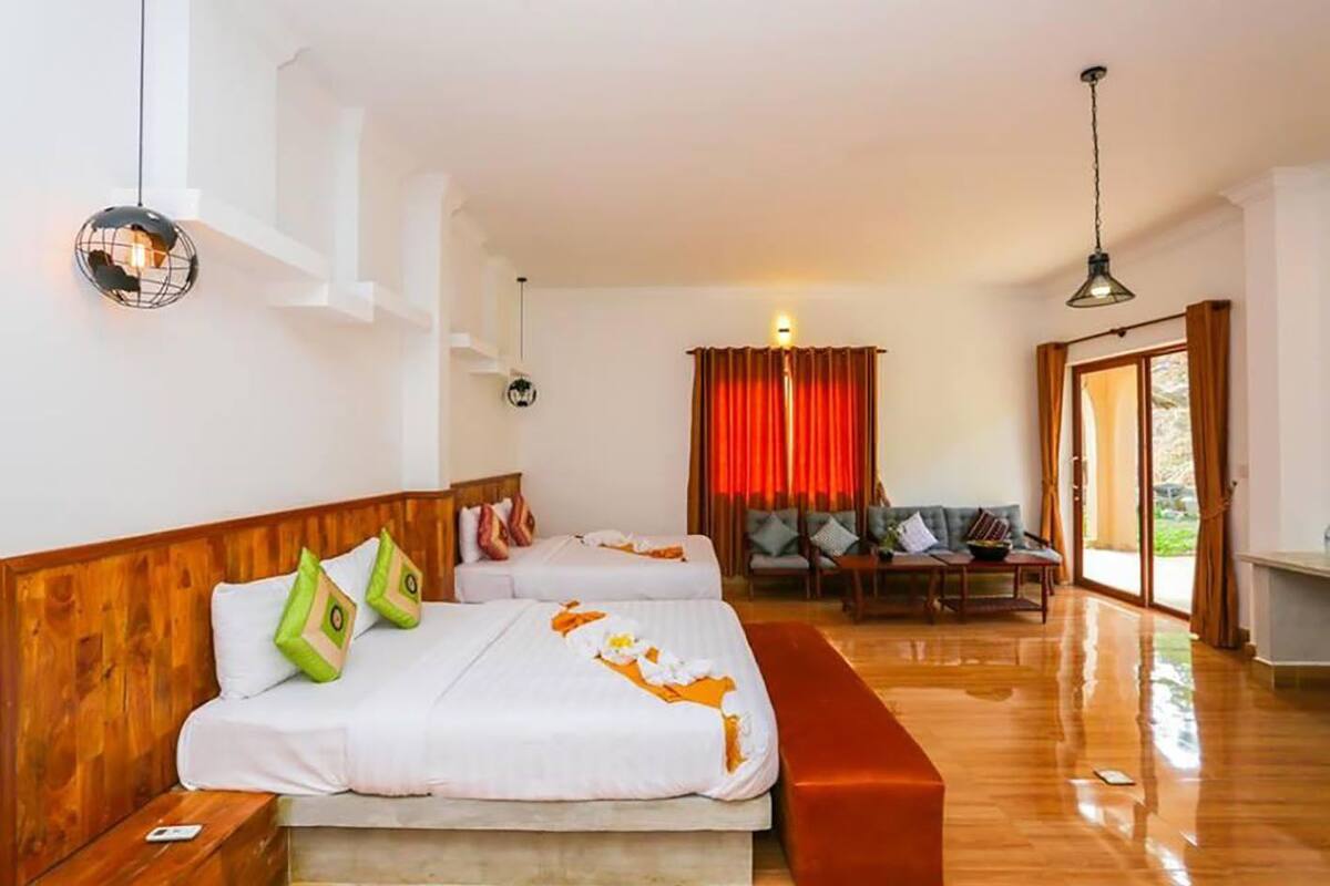 Ein Hotelzimmer mit zwei Betten, einem hölzernen Kopfteil, einer Bank, einer Couch und einem Esstisch.