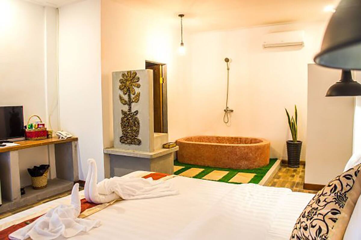 Ein Hotelzimmer mit Bett, Schminktisch mit Spiegel, Badewanne, Fernseher, Schreibtisch und einer Topfpflanze.