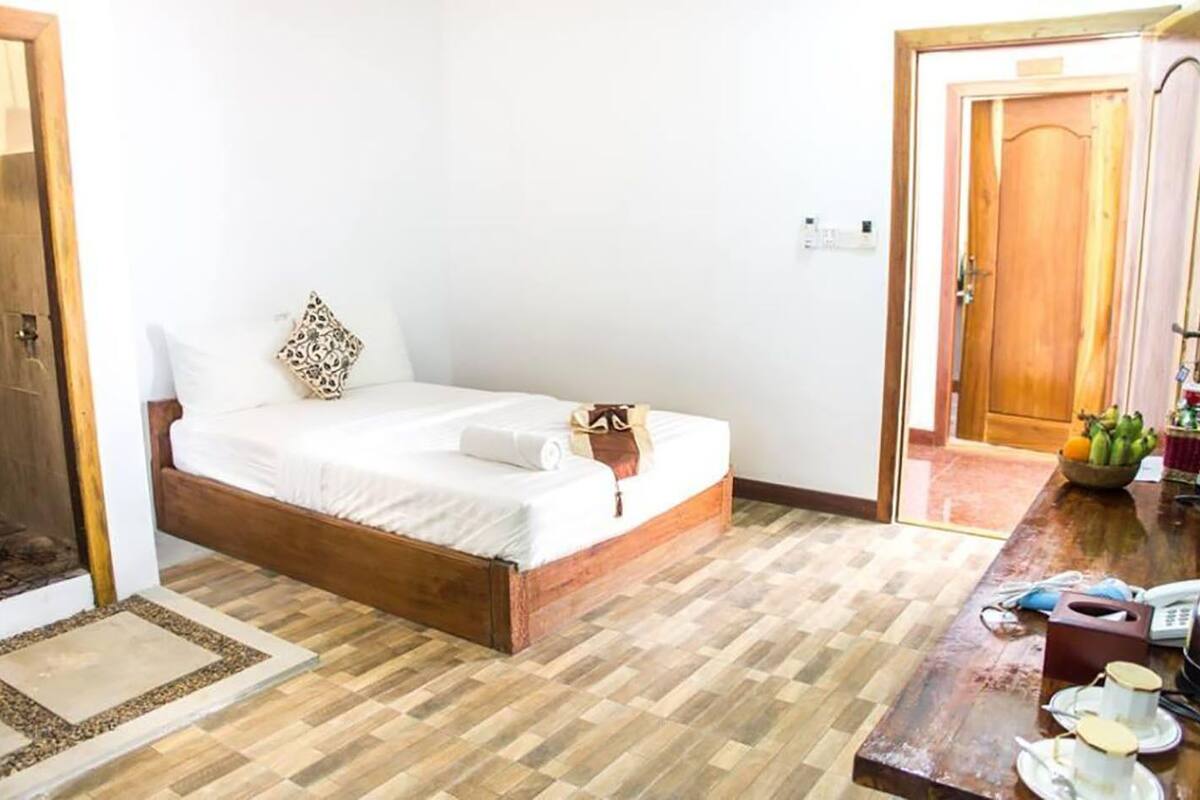 Ein Schlafzimmer mit einem Holzbett, weißer Bettwäsche, einem kleinen Nachttisch mit einer Obstschale und einer Holztür.