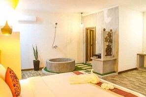 Habitación de hotel con cama, bañera de piedra, planta en maceta y espejo.