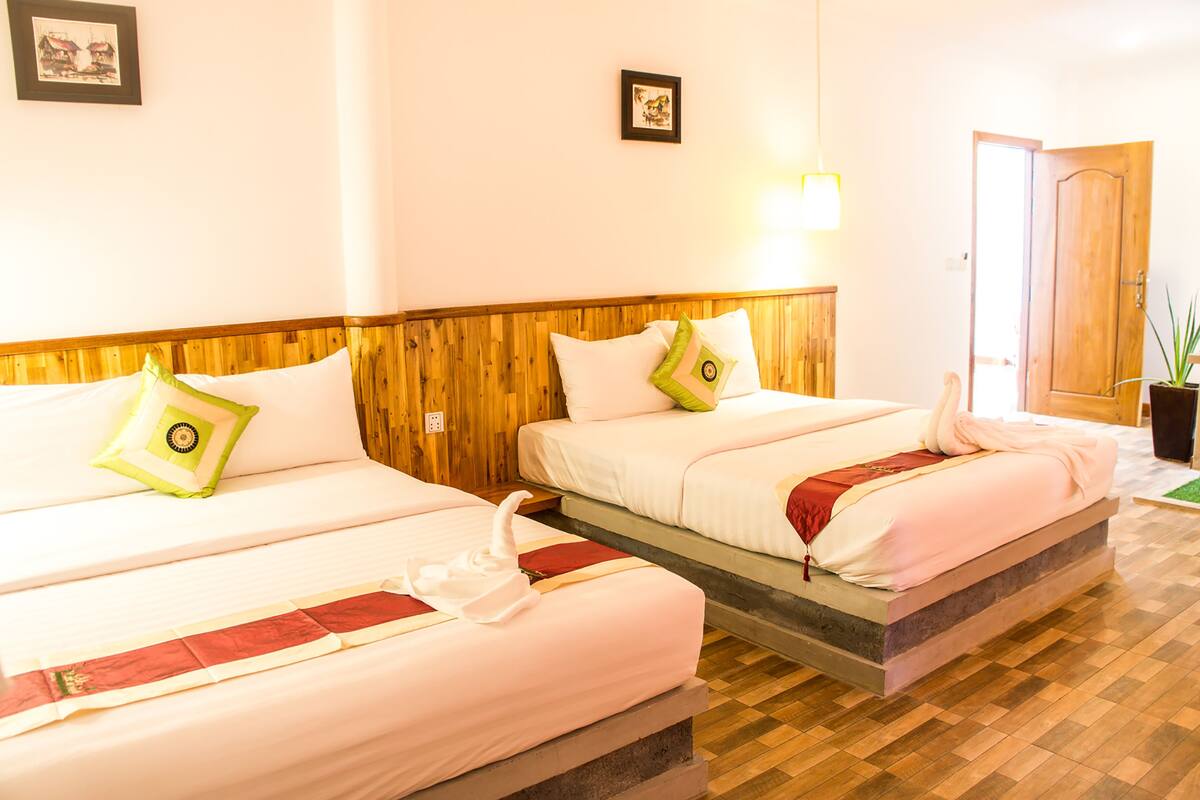 Ein Hotelzimmer mit zwei Betten, hölzernen Kopfteilen, weißer Bettwäsche und Holzboden.
