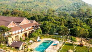 Un hotel con piscina, rodeado de exuberante vegetación y una montaña al fondo.