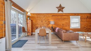 A cozy cabin interior with a dining table, chairs, a sofa, and a star decoration on the wall. - Secluded Pet-Friendly High-Tech Log Cabin in the Woods (Berkeley Springs)