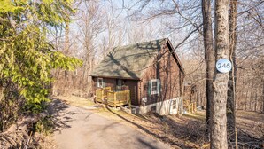 A rustic cabin with a wooden deck, surrounded by trees and a clear sky. - Secluded Pet-Friendly High-Tech Log Cabin in the Woods (Berkeley Springs)
