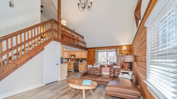A spacious living area with a wooden staircase, a leather sofa, and a dining table. - Secluded Pet-Friendly High-Tech Log Cabin in the Woods (Berkeley Springs)