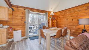 A cabin interior with a wooden interior, a dining area with a table and chairs, a small kitchenette, and a cozy seating area with a sofa. - Secluded Pet-Friendly High-Tech Log Cabin in the Woods (Berkeley Springs)