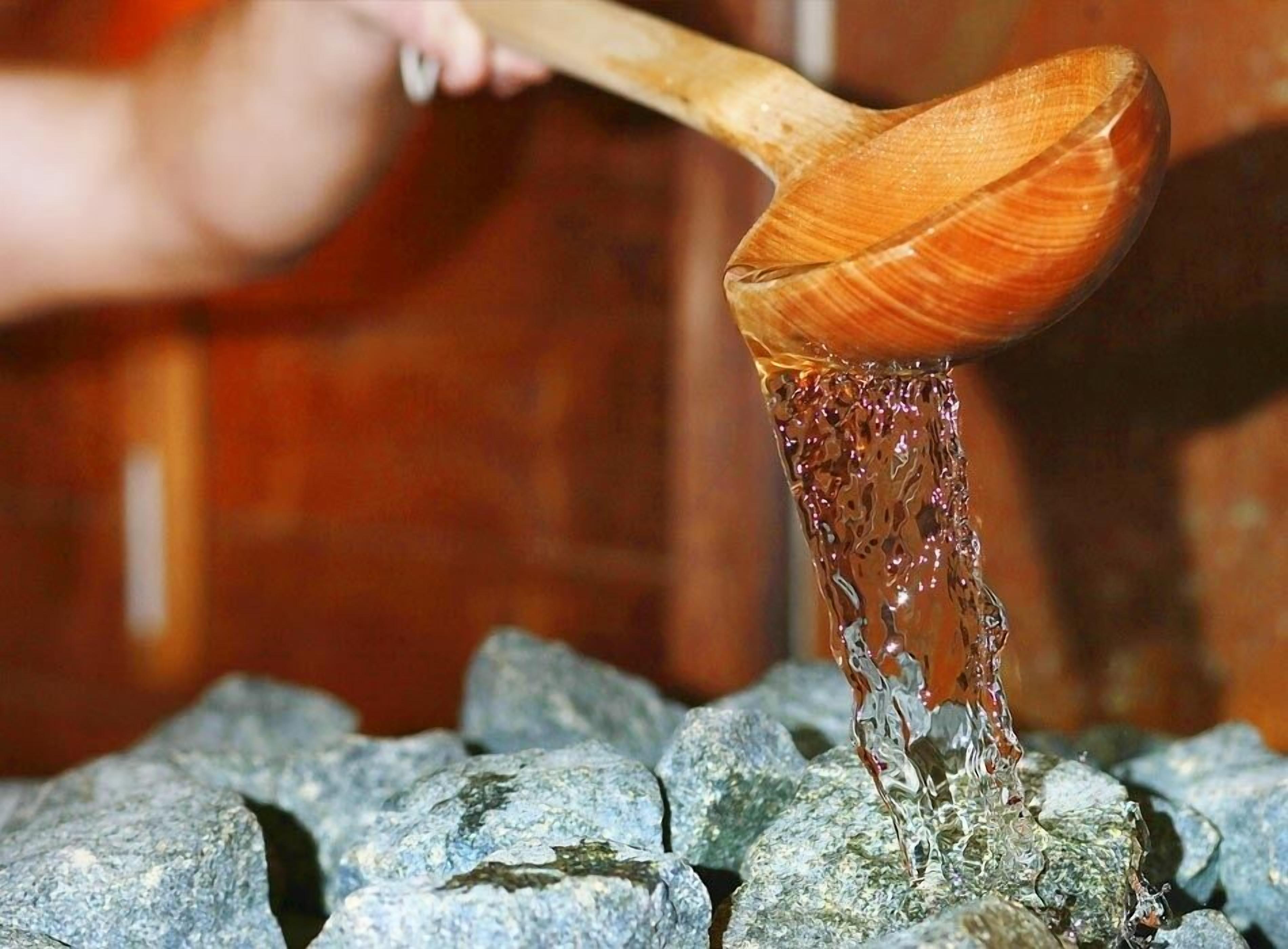 A wooden ladle pouring liquid over rocks.