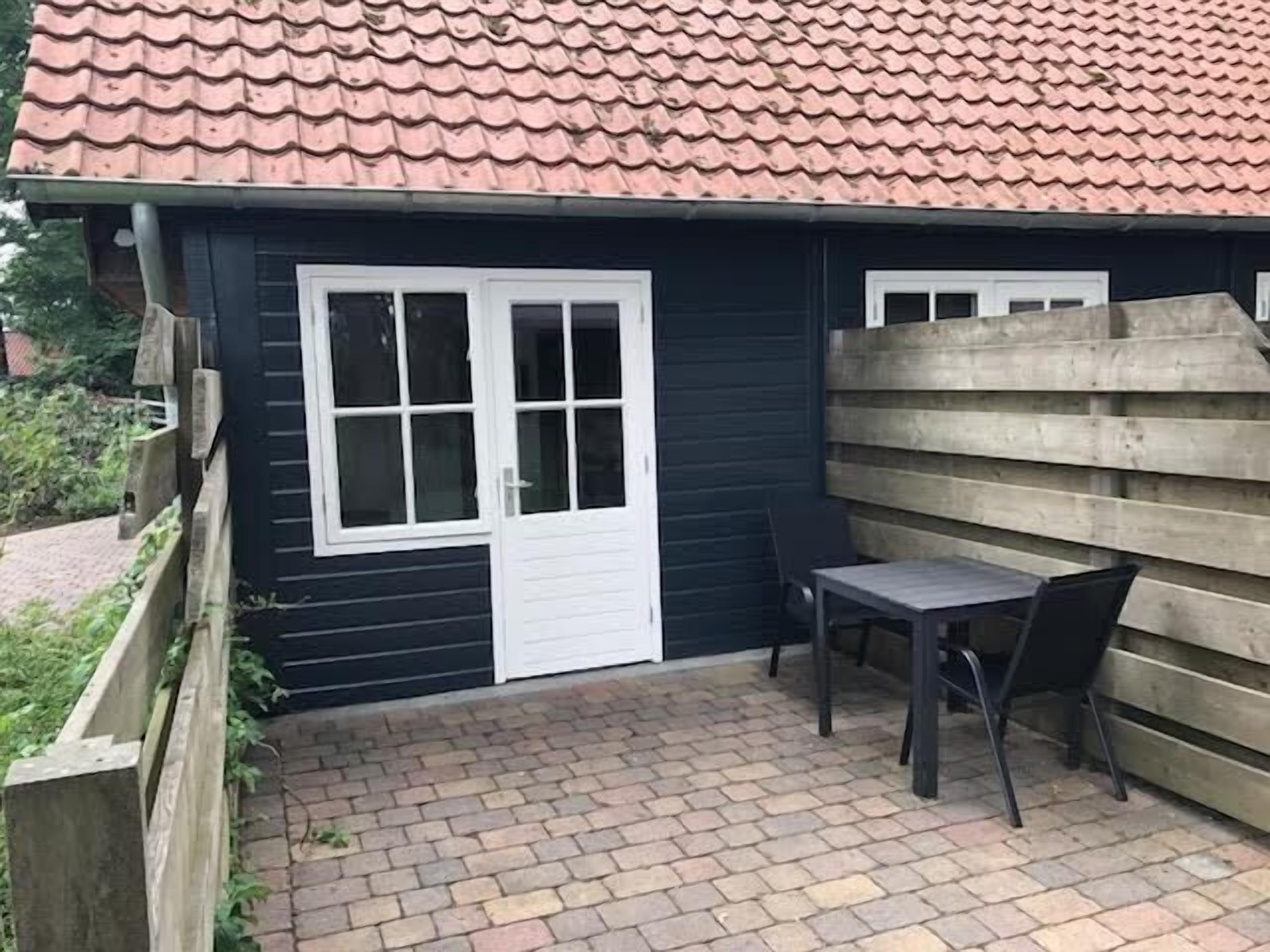 En lille bygning med et tagtækket tag, en dør og et bord med stole udenfor.
