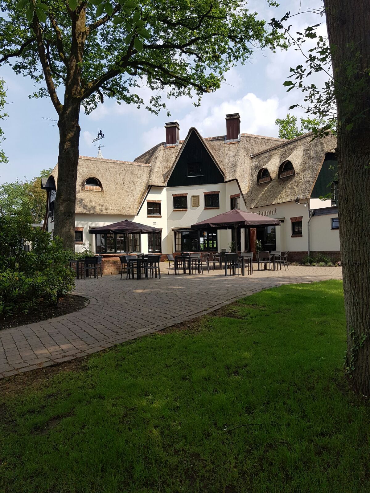 Un edificio tradicional con techo de paja, un patio con mesas al aire libre y un césped bien cuidado.