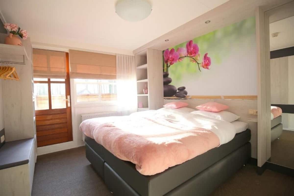 Un dormitorio con cama, armario, espejo y un cuadro de flores en la pared.