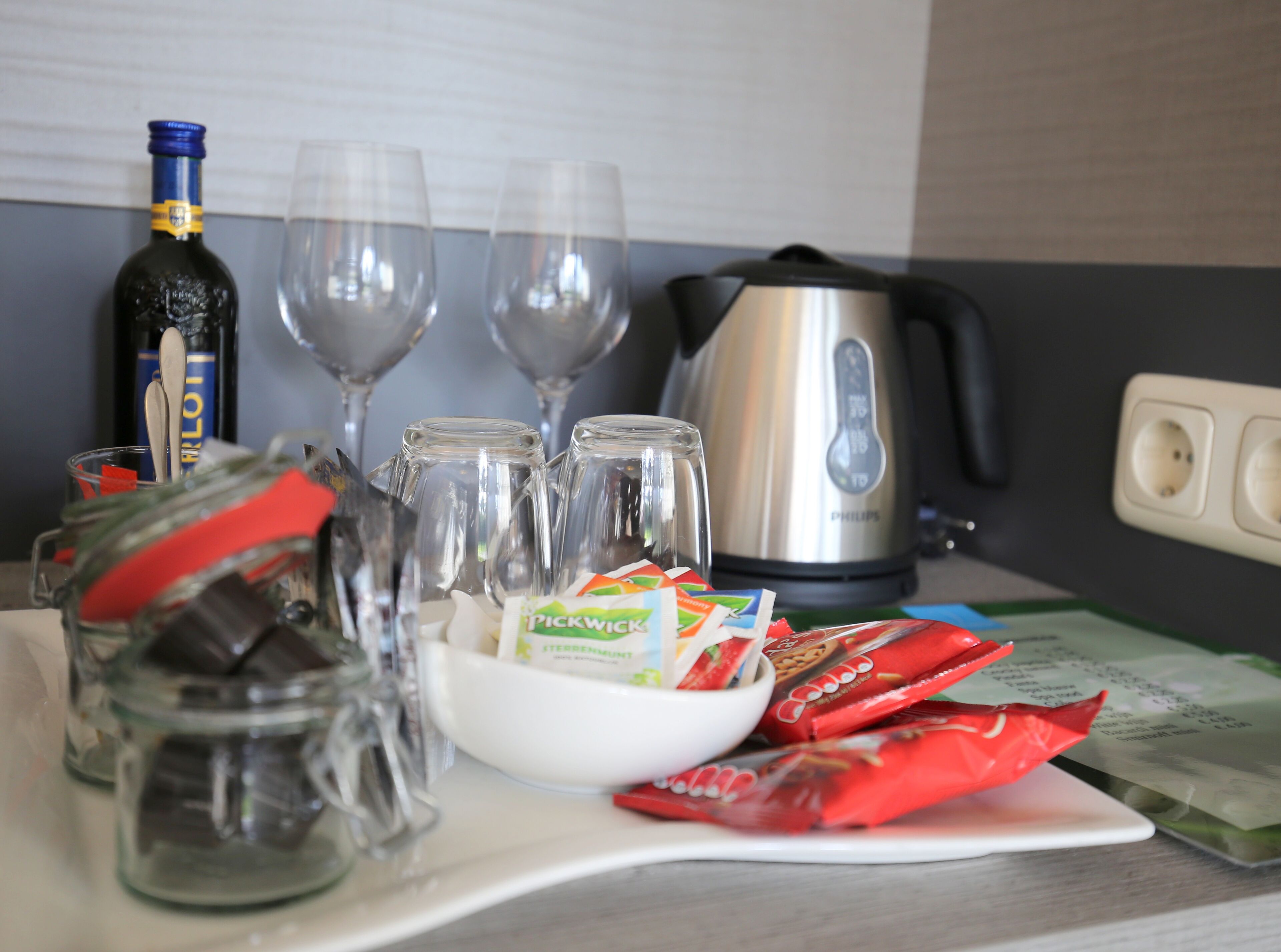 Un comptoir de cuisine avec une bouteille, deux verres à vin, une bouilloire et divers aliments.