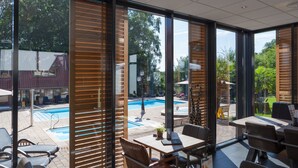 A modern outdoor dining area with a pool view, wooden blinds, and comfortable seating. - Huize Hölterhof (Enschede)