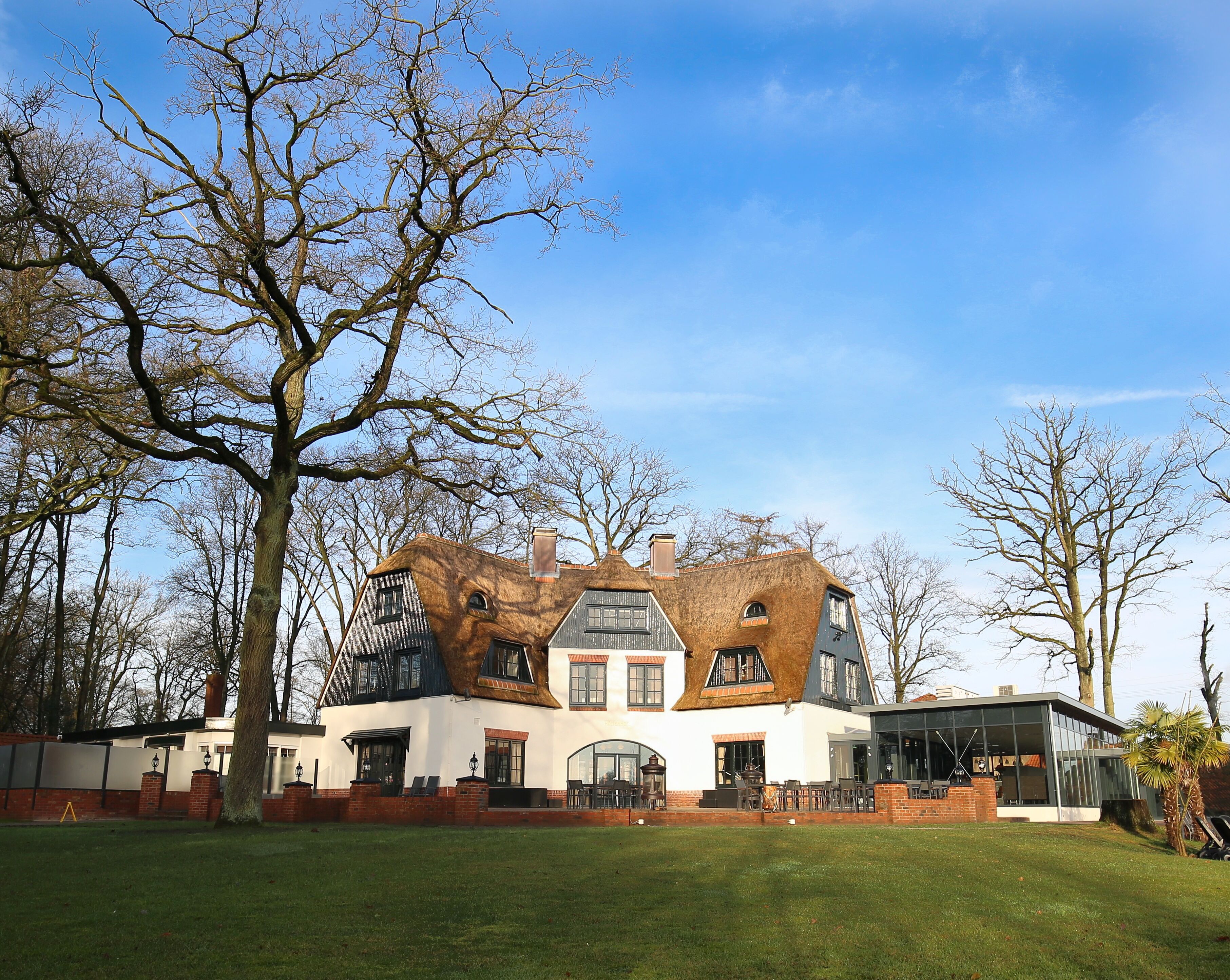 A large, two-story house with a unique, asymmetrical roof design, surrounded by a well-maintained lawn and trees.