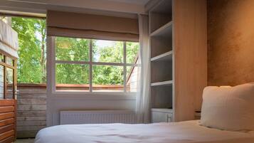 A bedroom with a large window, wooden slatted walls, a white radiator, and a bed with white bedding.