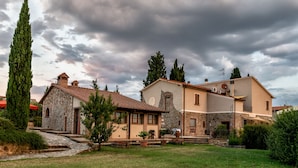 A two-story stone house with a stone facade, a tiled roof, and a small garden with potted plants. - Agriturismo Signorini (Lajatico)