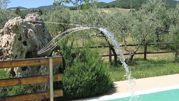 A pool with clear water, a wooden fence, and a rocky outcrop in the background. - Agriturismo Signorini (Lajatico)