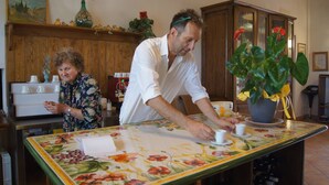 A kitchen with wooden cabinets, a table with a floral tablecloth, and a potted plant. - Agriturismo Signorini (Lajatico)