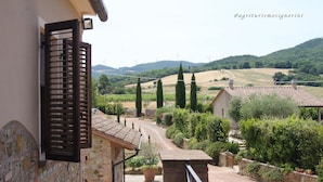 A stone building with a balcony, a gate, and a view of a rural landscape with wind turbines and rolling hills. - Agriturismo Signorini (Lajatico)