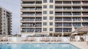 A multi-story hotel with a swimming pool, outdoor seating, and balconies. - Island Winds East 505 by Liquid Life (Gulf Shores)