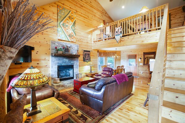 A cozy cabin interior with a fireplace, leather sofa, and a wooden staircase. - New Kitchen, EV charging, great reviews
3 levels, privacy2 fireplaces,hottub (Hiawassee)