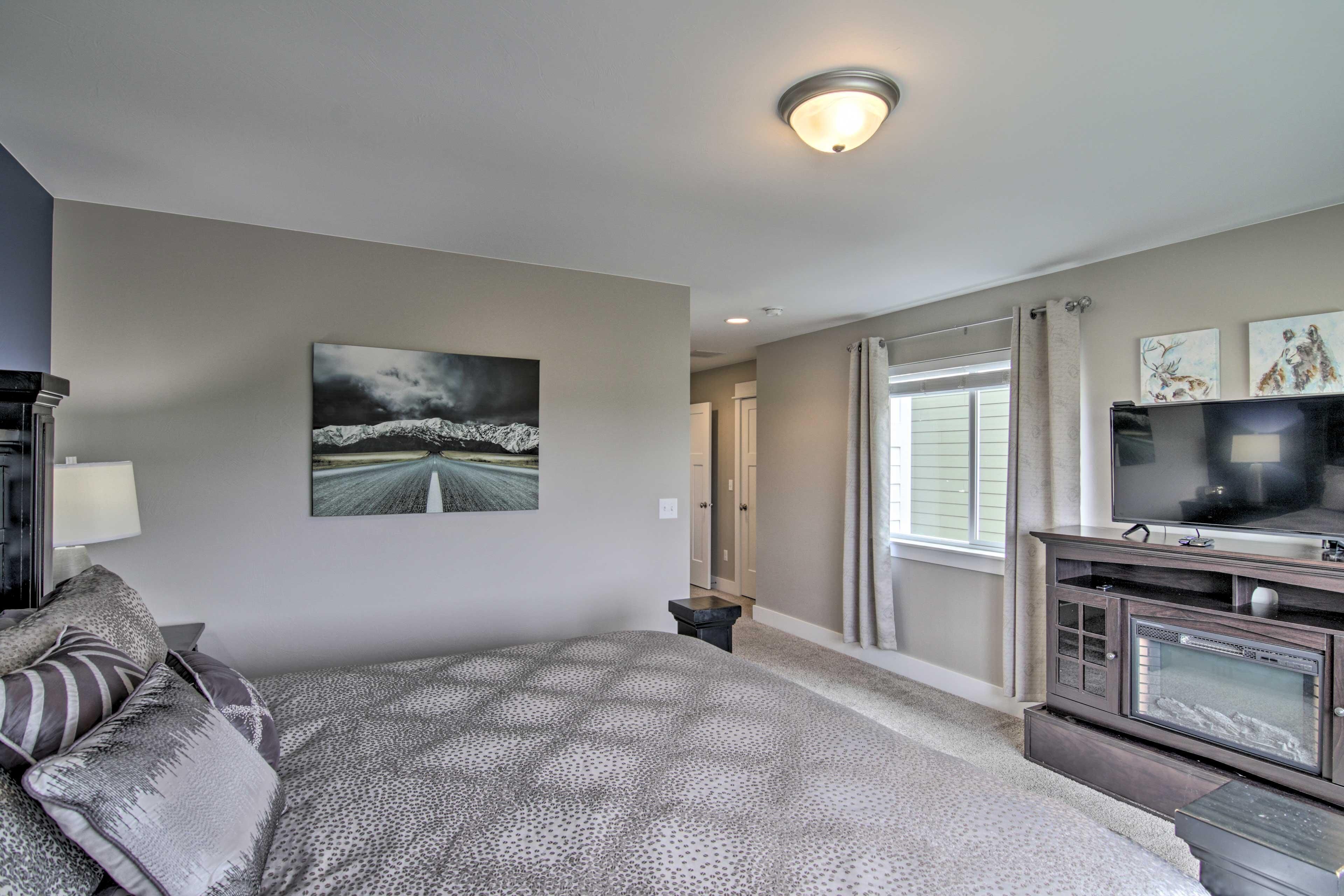 A bedroom with a bed, a television, a painting, and a window with curtains.