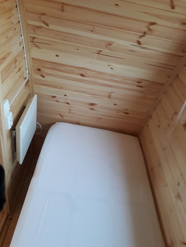 Ein kleiner, schmaler Raum mit Holzwänden und einer weißen Matratze.