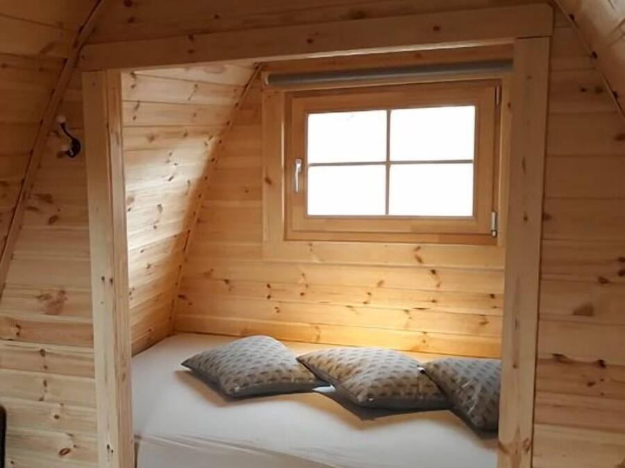 Eine kleine, hölzerne Blockhütte mit Schlafzimmer im Blockhausstil, inklusive Fenster und zwei Kissen.