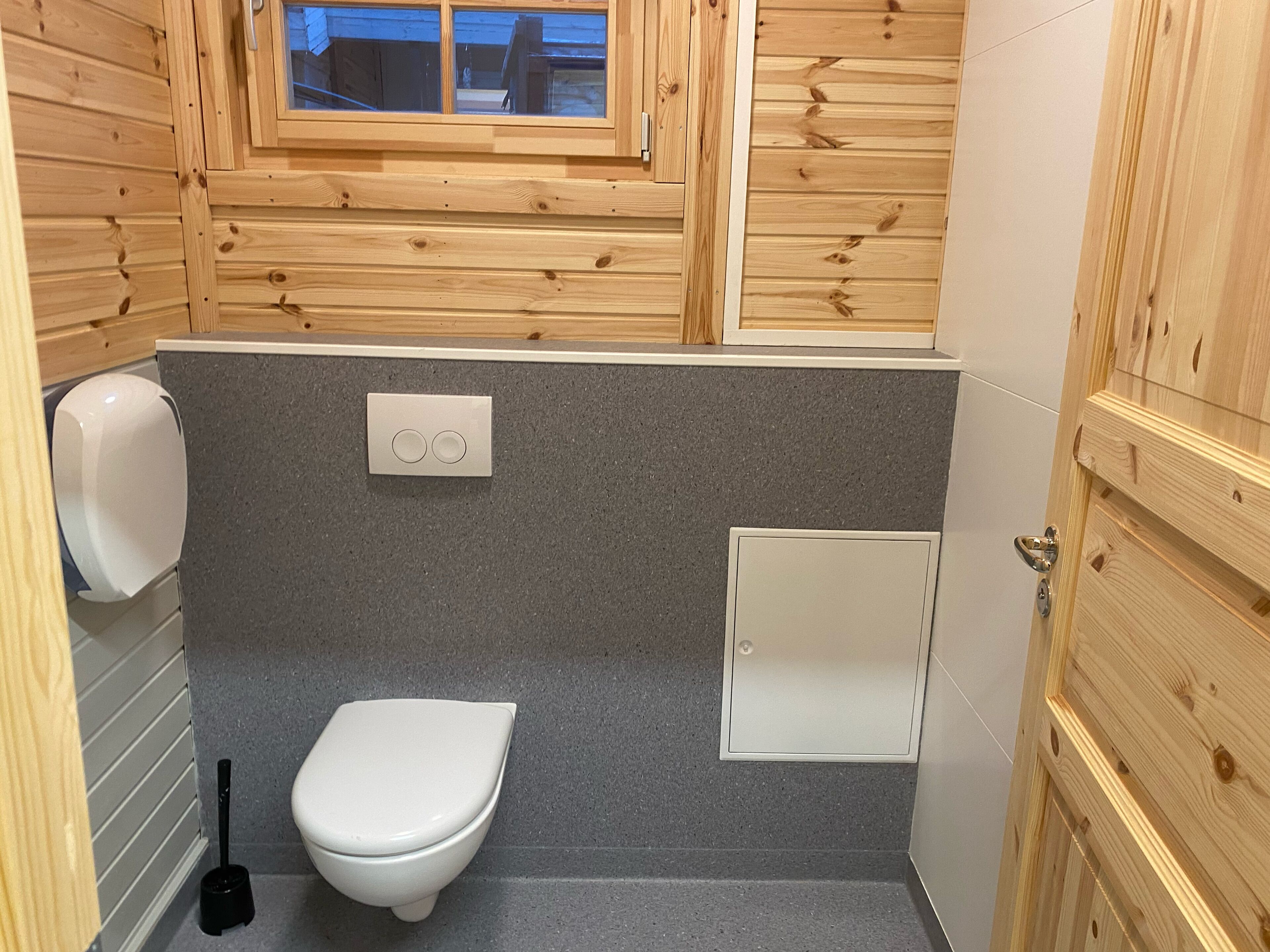 Ein kleines, kompaktes Badezimmer mit Holzvertäfelung, einer Toilette, einem Handtrockner und einem Fenster.