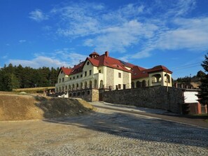 Ein großes, historisches Gebäude mit mehreren Bögen und einem roten Dach, umgeben von einer Steinmauer und einem Pflasterweg.