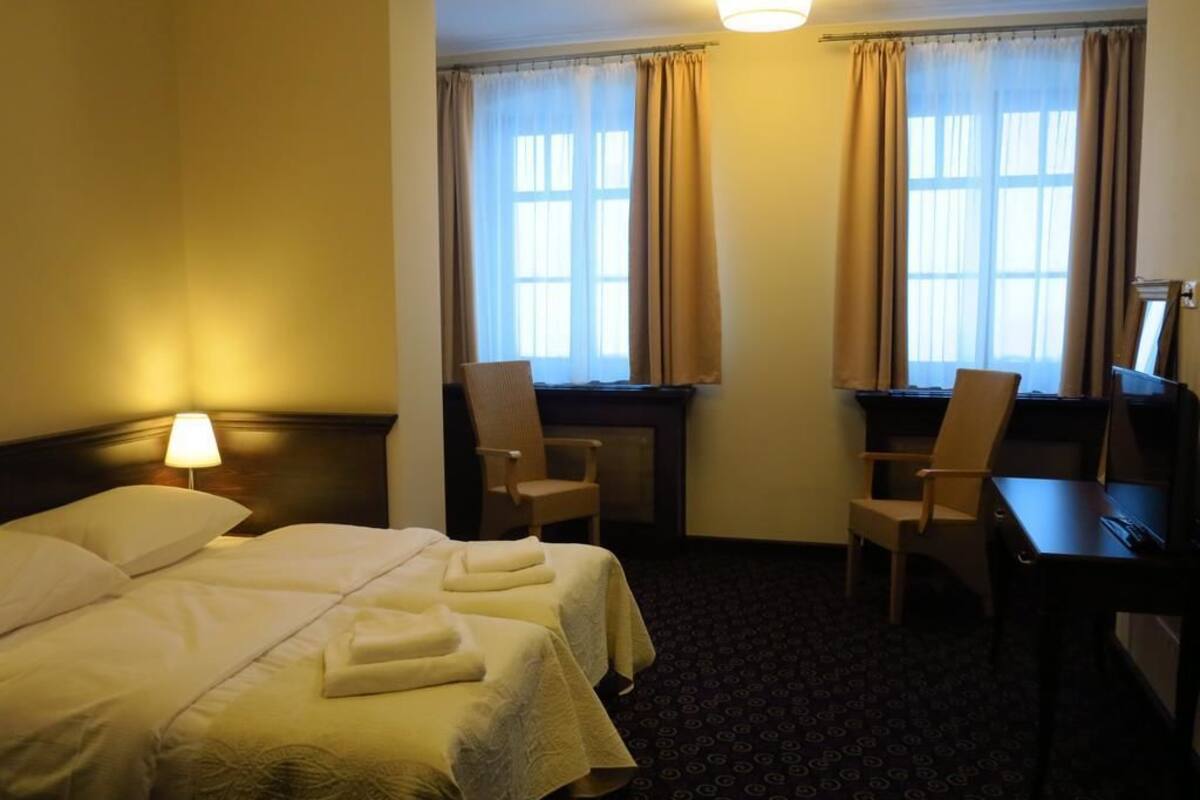 A hotel room with a large bed, two chairs, a desk, and a window with curtains.