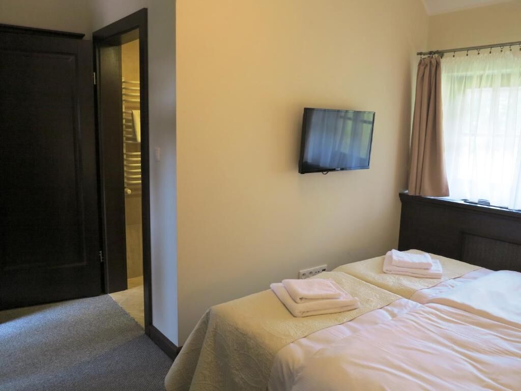 A hotel room with a bed, a television mounted on the wall, and a door leading to another room.