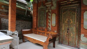 A wooden bench with intricate carvings, a stone bench, and a large ornate door with a floral design. - Pering Bungalow Ubud (Ubud)
