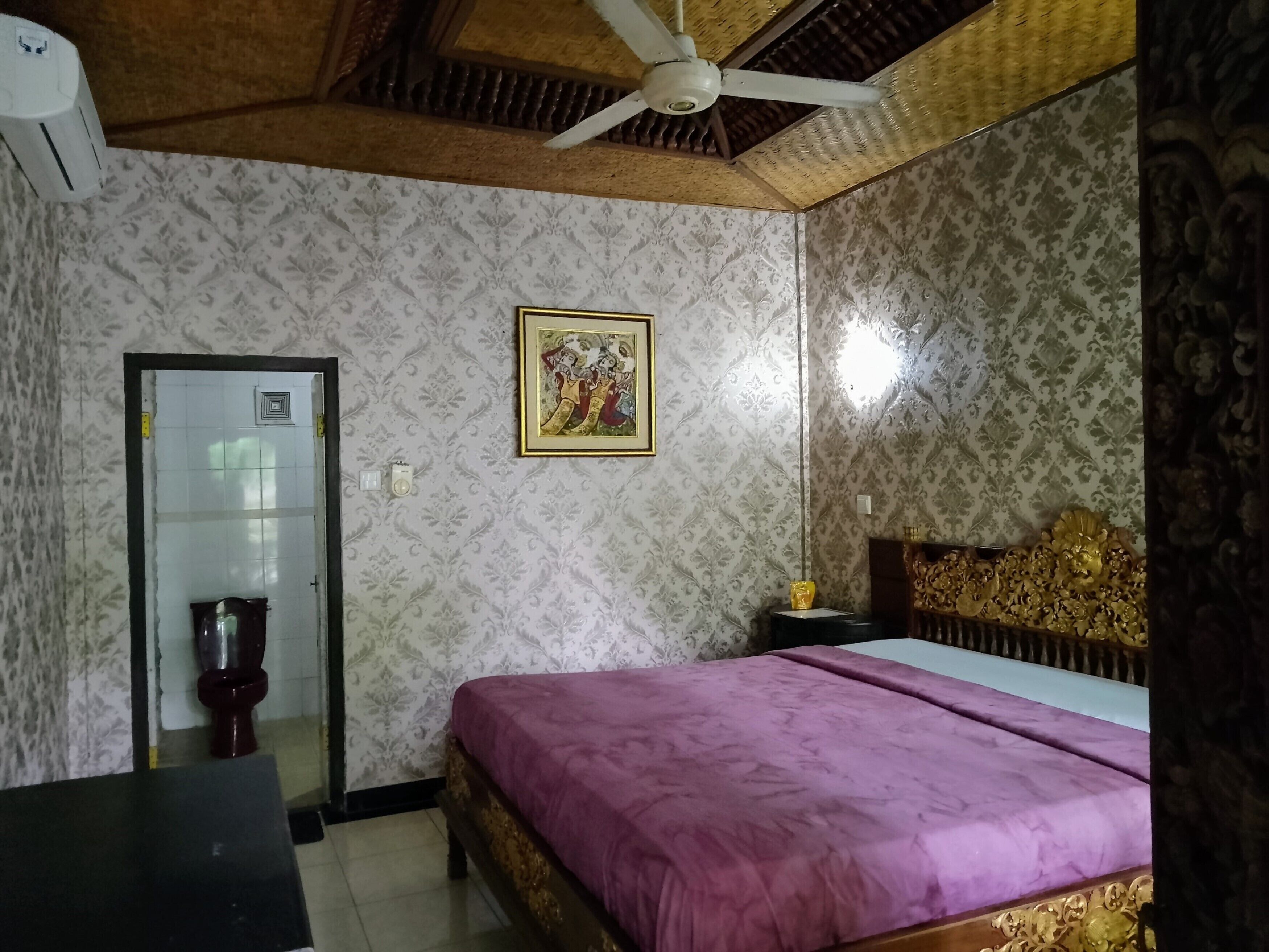 Ein Schlafzimmer mit einem Bett, einem Deckenventilator, einer Tür und einem an der Wand hängenden Bild.