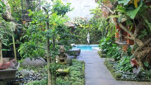 A wooden pathway leading to a pool surrounded by lush greenery and stone statues. - Pering Bungalow Ubud (Ubud)