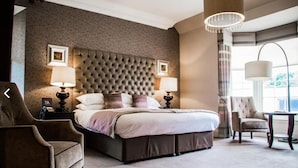 A hotel room with a large bed, two bedside lamps, a tufted headboard, a chair, and a table. - Dumfries Arms Hotel (Cumnock)