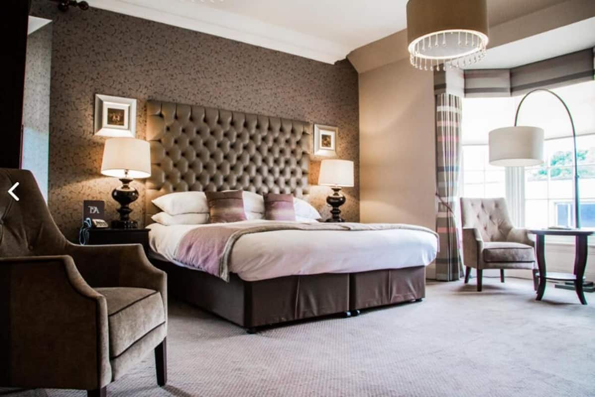 A hotel room with a large bed, two bedside lamps, a tufted headboard, a chair, and a table.