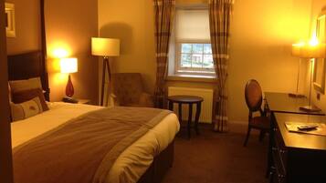 A hotel room with a large bed, a desk, a chair, a small table, and a window with curtains.