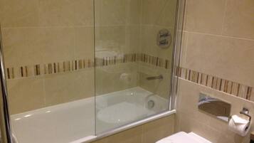 Un baño con bañera de hidromasaje con mampara de vidrio, inodoro y perchero para toallas.