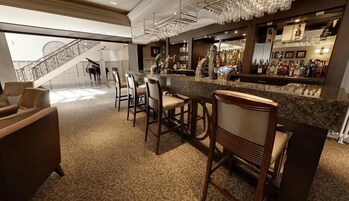 Uma área de bar com bancada de mármore, banquetas e uma escadaria ao fundo.