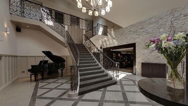 A grand staircase with a piano, a round table with a vase of flowers, and a stone wall. - Dumfries Arms Hotel (Cumnock)
